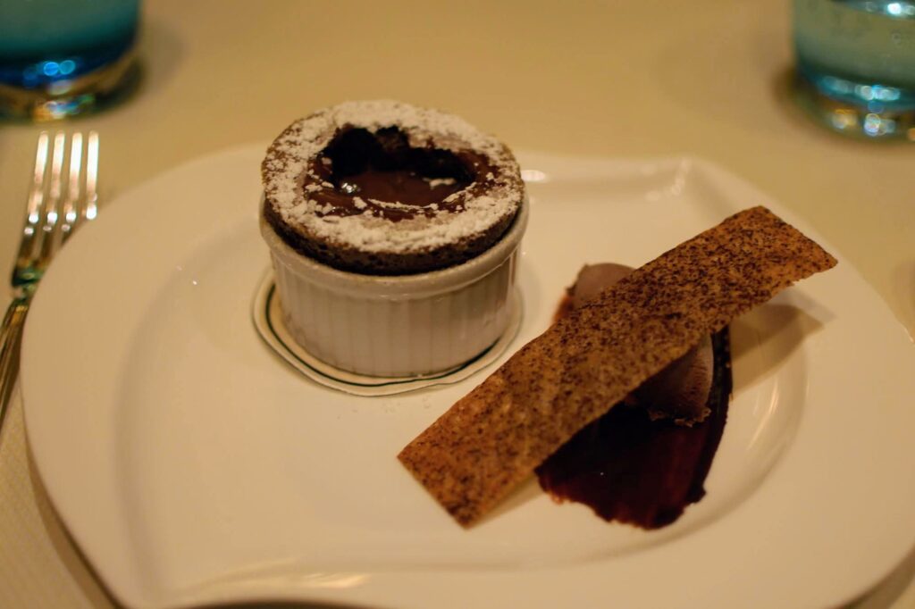 Hawaiian Cona Chocolate Souffle served with a choclate tuile and chocolate ganache, chocolate soil, with chocolate sauce poured into the souffle