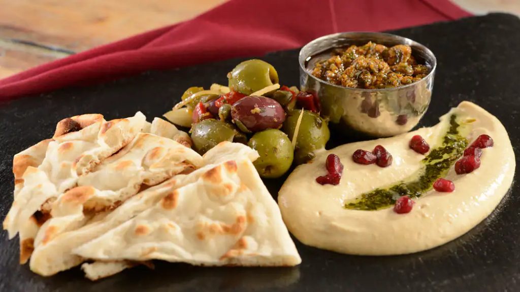 A plate filled with olives, pita bread, hummus and a dipping sauce - Spice Road Table